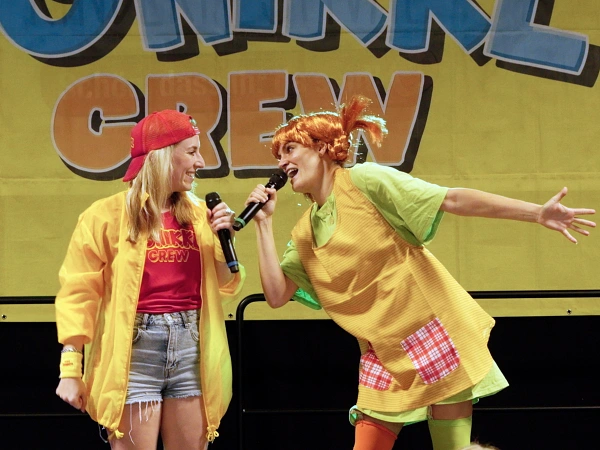 Zwei Sängerinnen der DONIKKL Crew singen gemeinsam auf der Bühne bei einem Mitmach-Kinderkonzert.